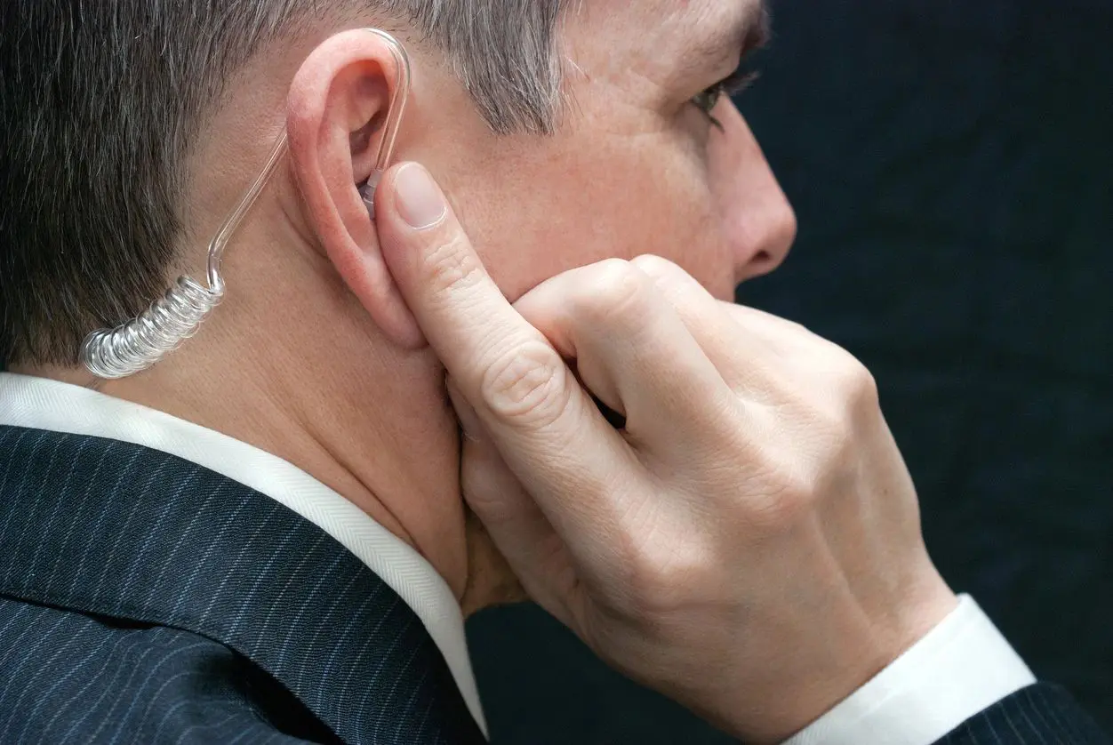 A man wearing an ear piece while holding his hand to the side of his face.